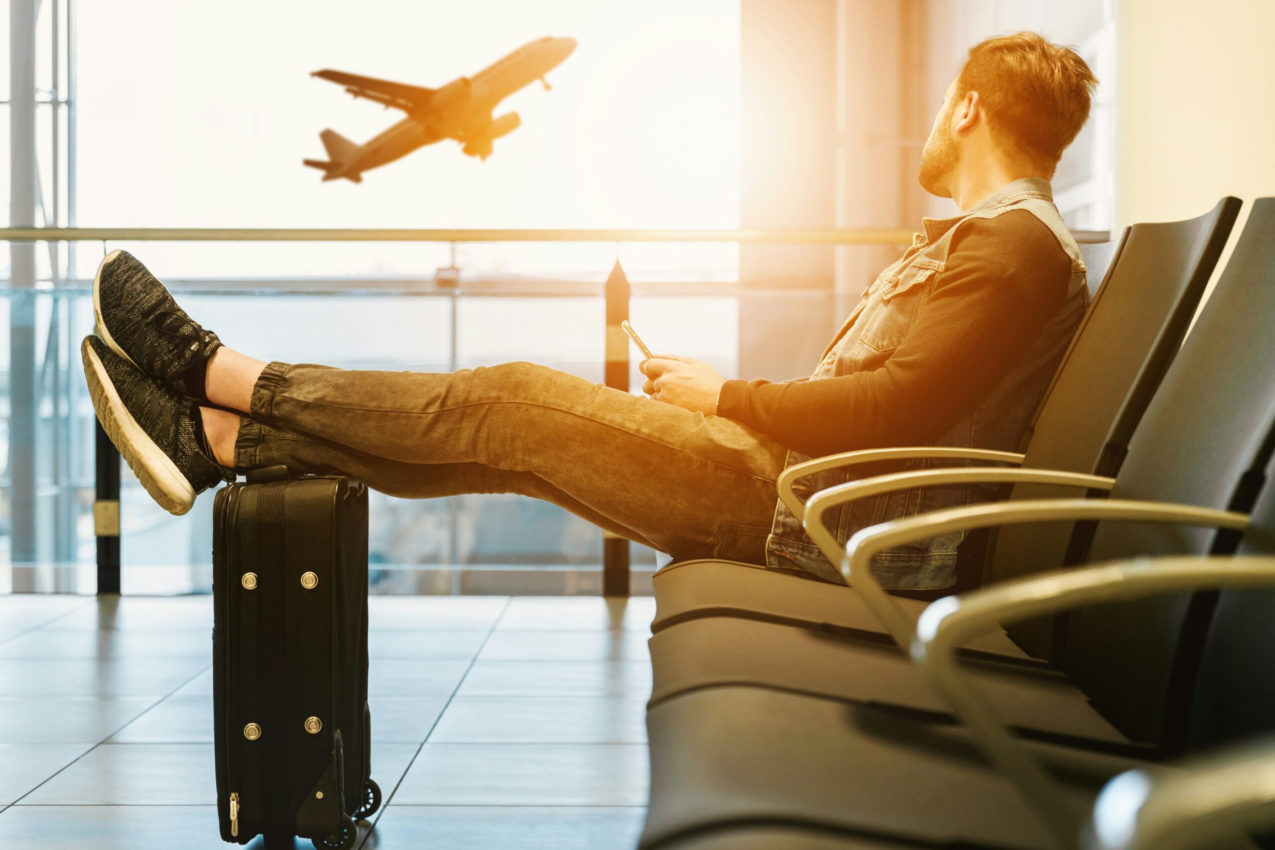 Traveller sitting at airport gate with luggage watching aircraft on tarmac